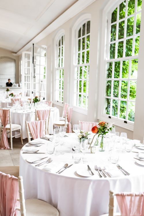 Photo of Orangery set for a wedding breakfast. Limewash chivari chairs draped in pink sashes